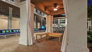 Un espace extérieur aménagé en patio, avec une table et des bancs en bois, des piliers en pierre et un ventilateur de plafond.