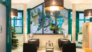 En entréhall med ett stort fönster med målat glas, svarta sittmöbler och en julgran.