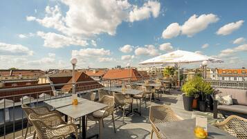 Une terrasse sur le toit, aménagée avec des tables et des chaises, des plantes en pot et un grand parasol.
