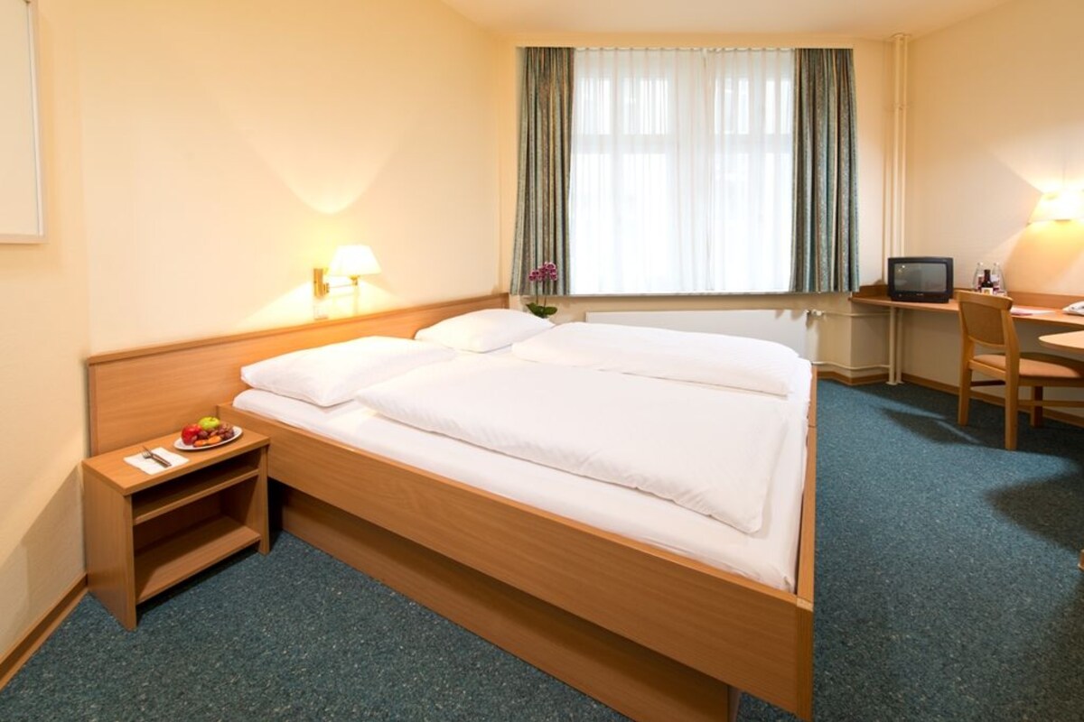 Une chambre d’hôtel avec un lit en bois, un bureau avec un ordinateur, une chaise et une petite table sur laquelle se trouve une assiette de fruits.