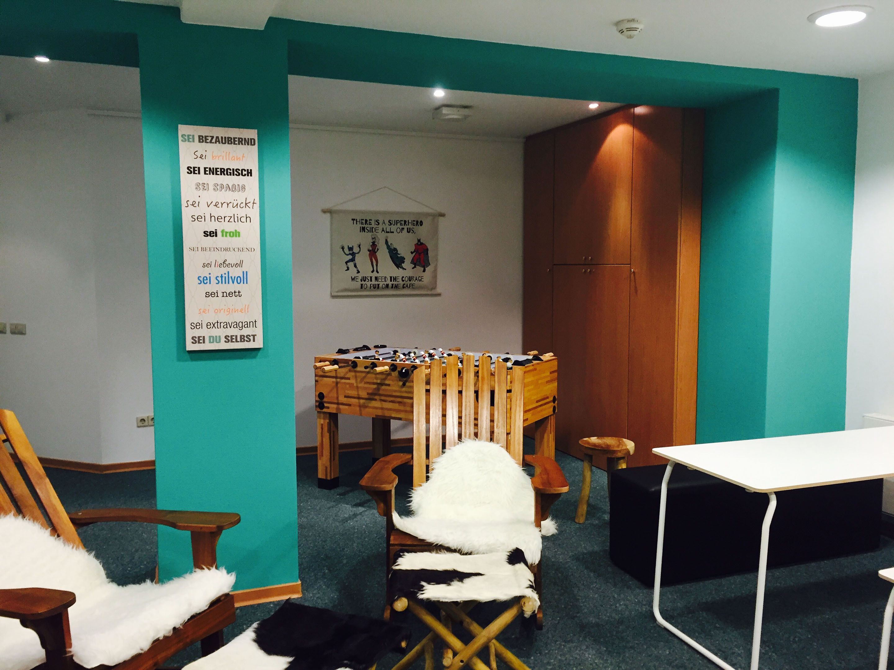 A room with teal walls, a wooden cabinet, a foosball table, and a poster on the wall.