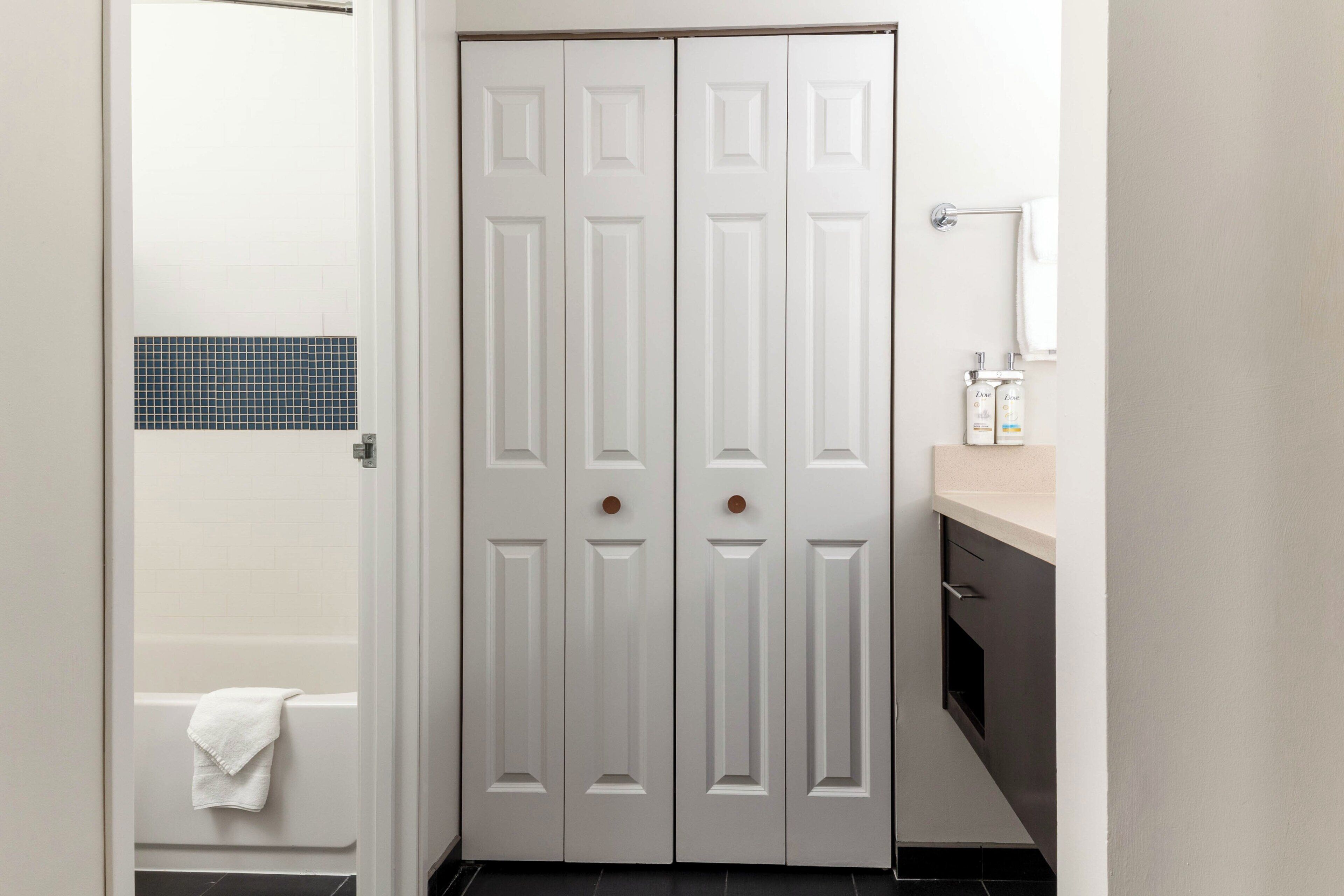 A bathroom with a white door, a bathtub, a towel, and a sink with a mirror.