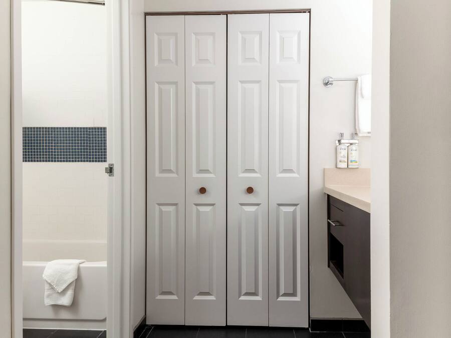 A bathroom with a white door, a bathtub, a towel, and a sink with a mirror.