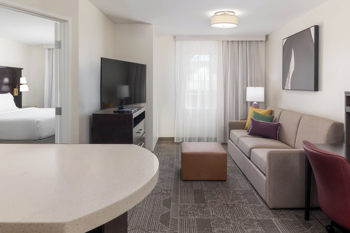 Een moderne hotelkamer met een bed, een televisie, een bank, een salontafel en een eettafel.
