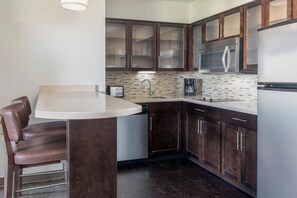 A modern kitchen with dark wood cabinets, a stainless steel microwave, and a built-in dishwasher. - Staybridge Suites Phoenix - Chandler by IHG (Chandler)