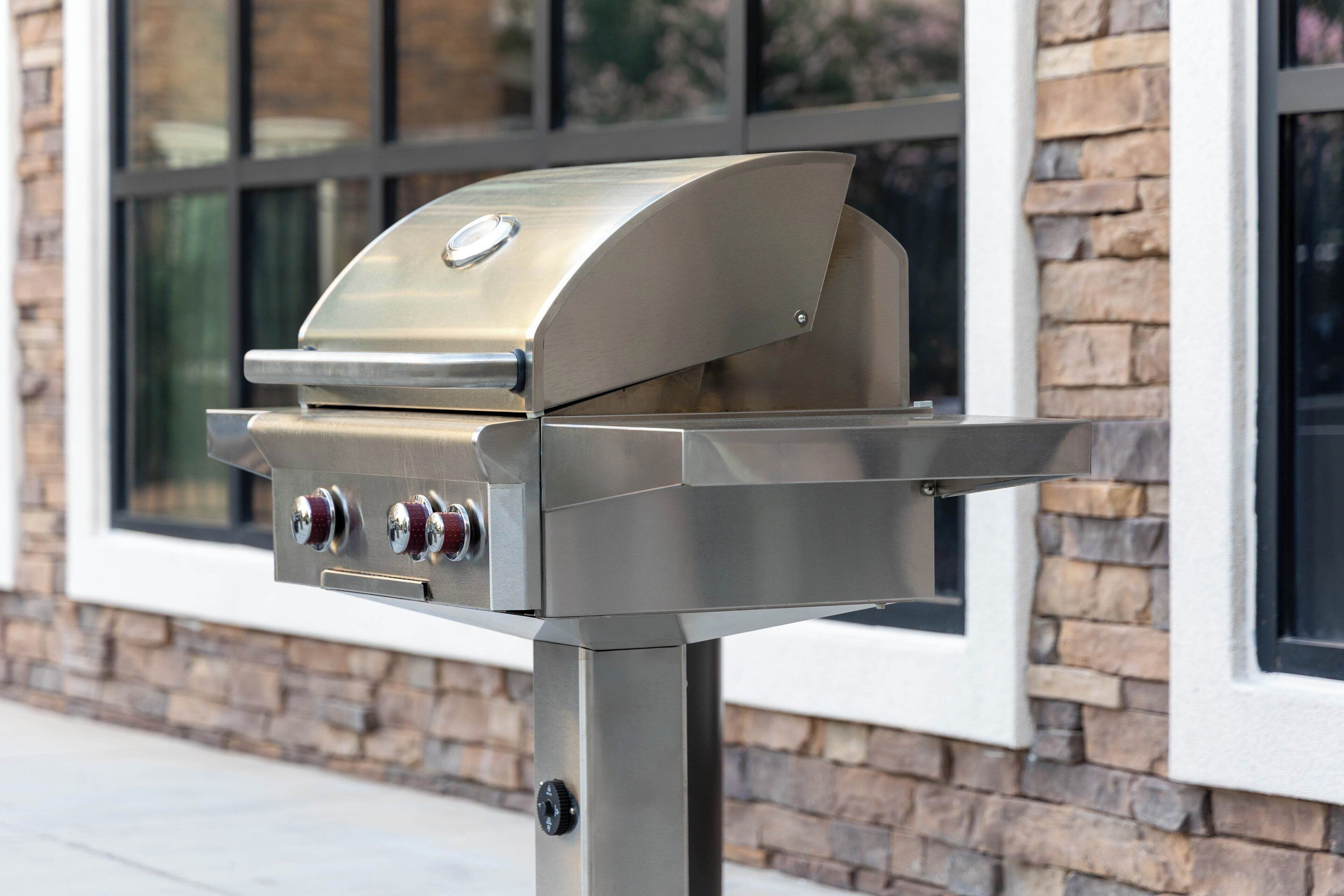 A stainless steel outdoor grill with two control knobs and a digital display, mounted on a metal stand.
