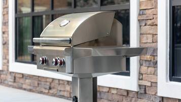 A stainless steel outdoor grill with two control knobs and a digital display, mounted on a metal stand.