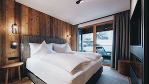 Un dormitorio moderno con pared de madera, una cama grande, una mesita pequeña y vistas del exterior a través de una puerta corredera.