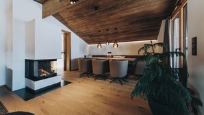 Una sala de estar moderna con chimenea, techo de madera y un comedor con sillas y una mesa.