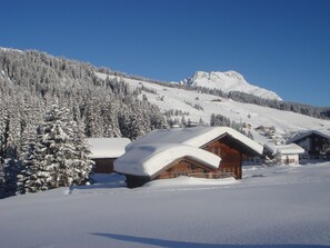 A snow-covered mountain with wooden cabins and a clear blue sky. - Balma Restaurant | Suites (Lech am Arlberg)