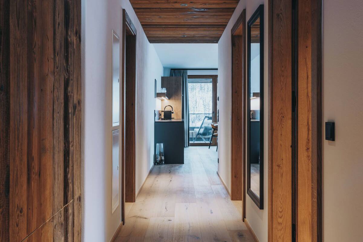 A hallway with wooden flooring and walls, leading to a kitchen area with a dining table and chairs.