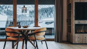 Un comedor con una mesa y sillas de madera, una chimenea y un amplio ventanal con vistas a una montaña nevada.