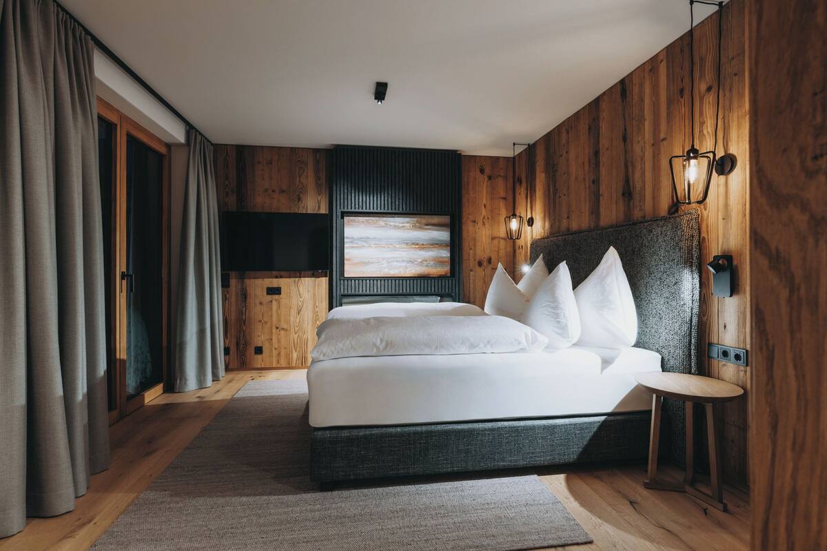 A modern bedroom with a large bed, wooden walls, a flat-screen TV, and a small side table.