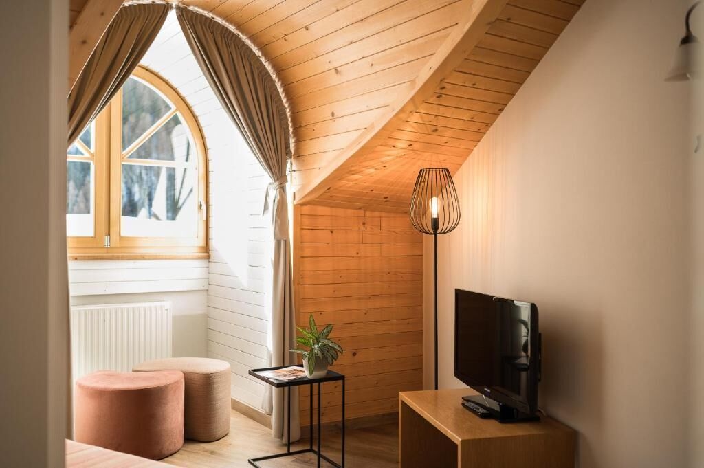 A cozy room with a sloped ceiling, a television, a small table with a plant, and two ottomans.