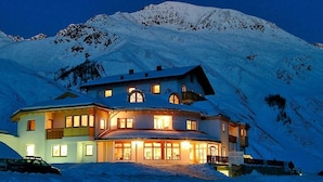 A large, multi-story building with multiple windows and a snow-covered mountain in the background. - Hotel Alpenjuwel (Curon Venosta)