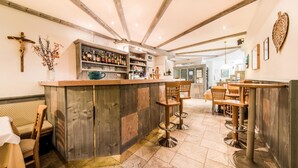 A bar area with wooden bar stools, a counter with various bottles, and a cross on the wall. - Hotel Alpenjuwel (Curon Venosta)