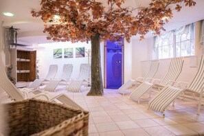 A spa area with striped lounge chairs, a large tree, and a blue-lit wall. - Hotel Alpenjuwel (Curon Venosta)
