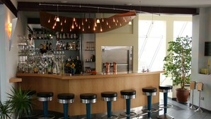 A bar area with a wooden counter, multiple stools, and a variety of bottles and glasses. - Hotel Sonnenhaken (Buschvitz)