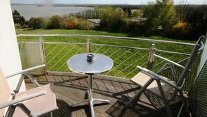 A balcony with a round table and chairs, overlooking a body of water and greenery. - Hotel Sonnenhaken (Buschvitz)