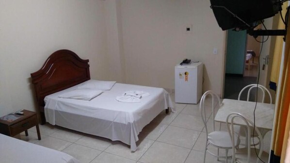 A small, clean room with a single bed, a small table, a chair, and a refrigerator. - Hotel Fátima (Divinopolis)