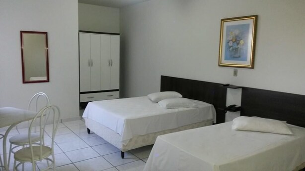 A hotel room with two beds, a desk, a chair, a wardrobe, and a framed picture on the wall. - Hotel Fátima (Divinopolis)