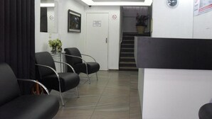 A reception area with a white reception desk, black chairs, a mirror, and a staircase leading to an upper level. - Hotel Fátima (Divinopolis)