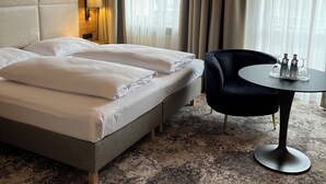 Une chambre d’hôtel avec un grand lit, une table ronde sur laquelle se trouvent deux bouteilles et des verres, une chaise et une lampe.