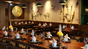 Un restaurant avec des tables en bois dressées pour le service, agrémentées de serviettes blanches, de verres à vin et d’assiettes.