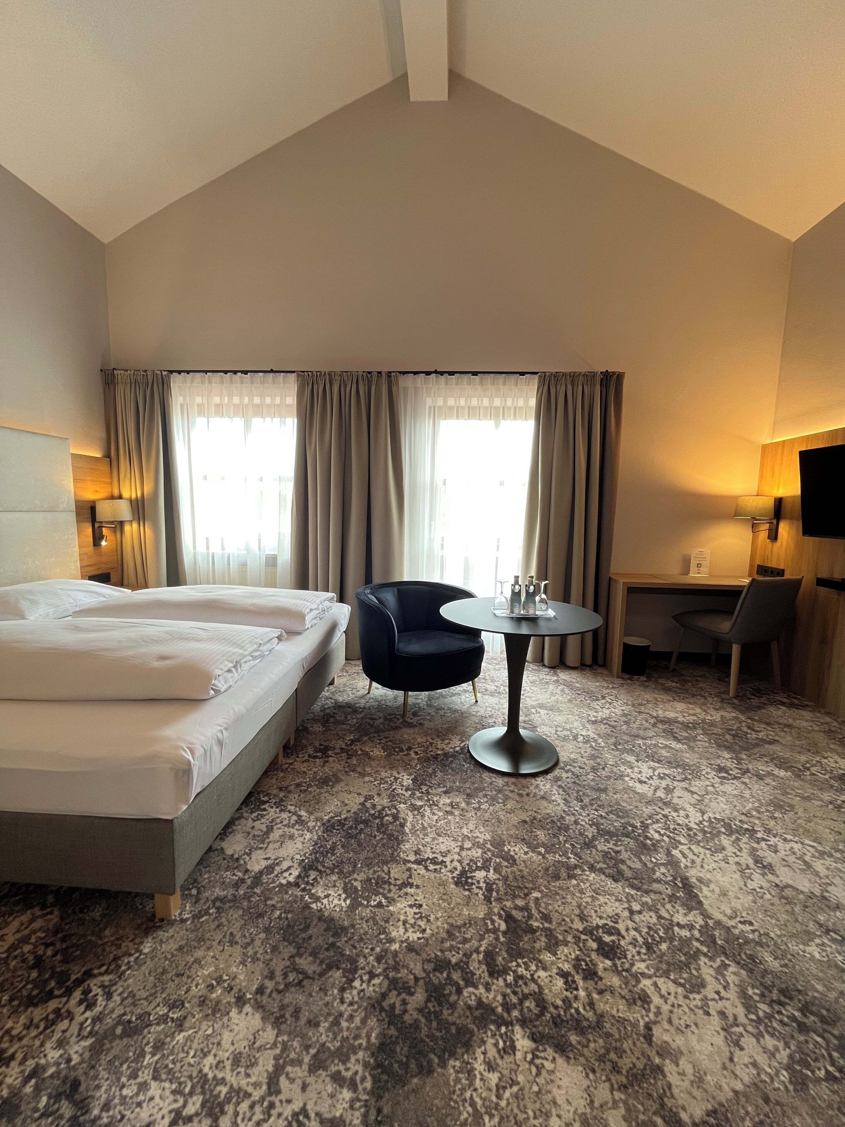 A hotel room with a large bed, a round table, a chair, and a desk.