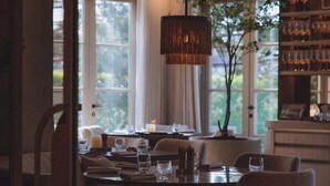 A dining area with a table set for four, a hanging light fixture, and a view of the outdoors. - Villa de Duinen (Noordwijk)