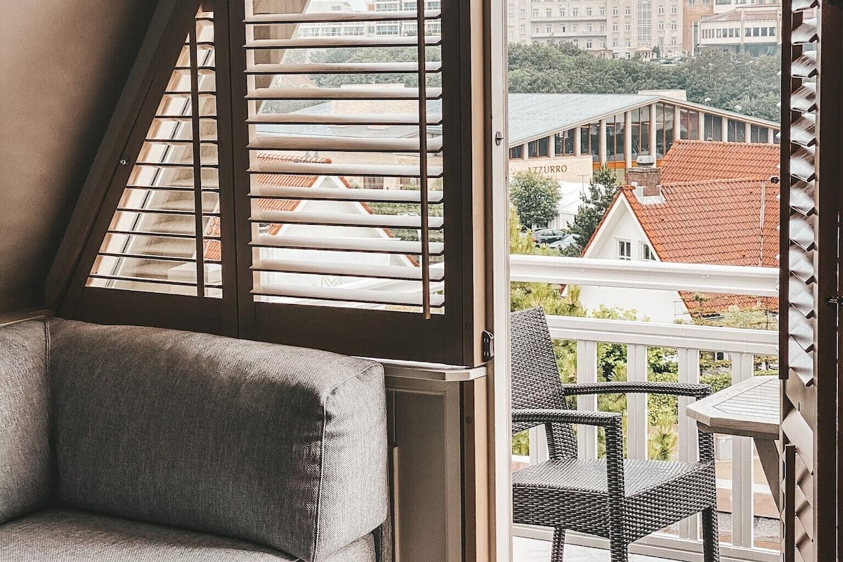 Un balcon avec un canapé et des fauteuils en osier, offrant une vue sur un paysage urbain avec des bâtiments et un ciel dégagé.