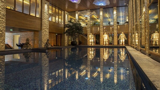 A spacious indoor pool area with a reflective floor, large windows, and modern lighting fixtures. - Villa de Duinen (Noordwijk)