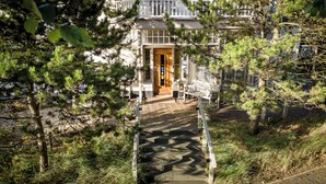 A building with a wooden door, a bench, and a paved pathway leading to the entrance. - Villa de Duinen (Noordwijk)