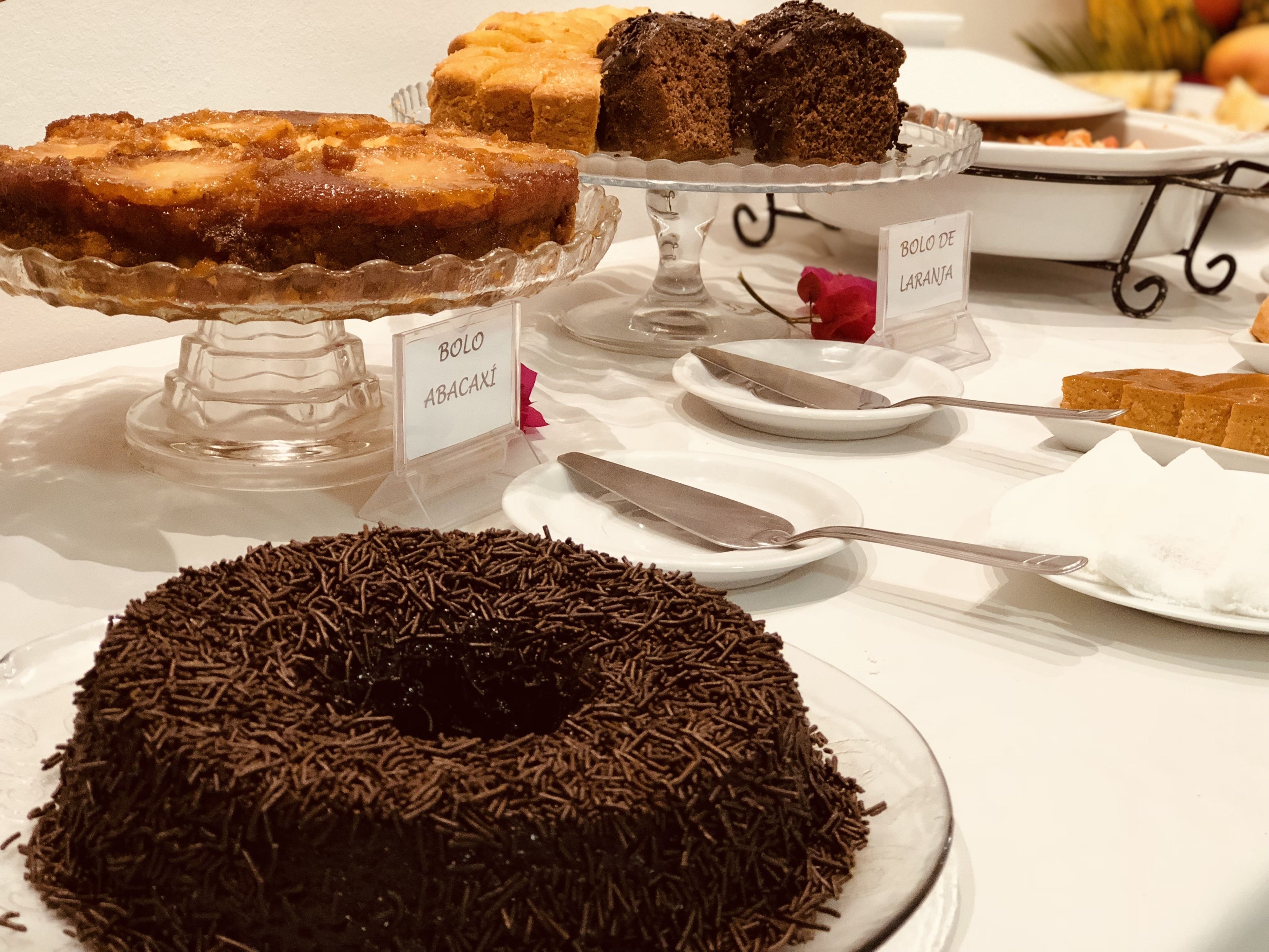 A dessert display with various cakes and pastries on glass stands, labeled with names.