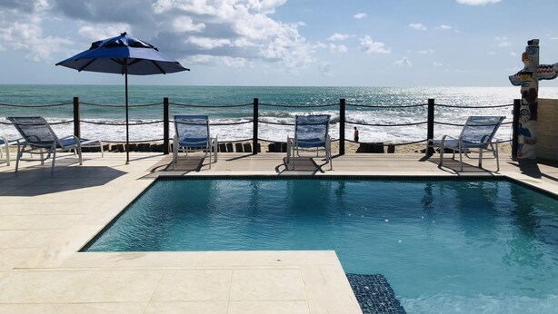 Zona de piscina con sillones reclinables y una sombrilla, con vistas al océano.