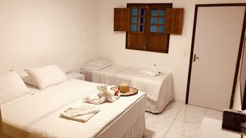 A hotel room with a large bed, a smaller bed, a vanity with a mirror, a wooden door, and a small table with a hat and towel.