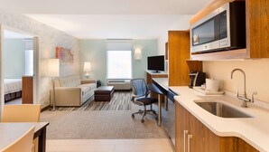A hotel room with a kitchenette, a bed, a sofa, a desk, and a TV. - Home2 Suites by Hilton Fargo, ND (Fargo)
