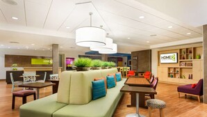 A modern hotel lobby with a green sofa, wooden tables, and a reception desk. - Home2 Suites by Hilton Fargo, ND (Fargo)