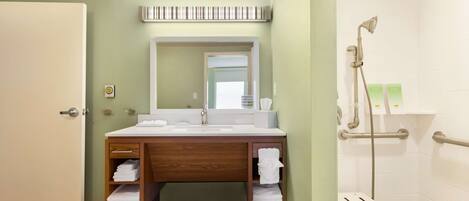 A bathroom with a wooden vanity, a mirror, a shower with grab bars, and a door.