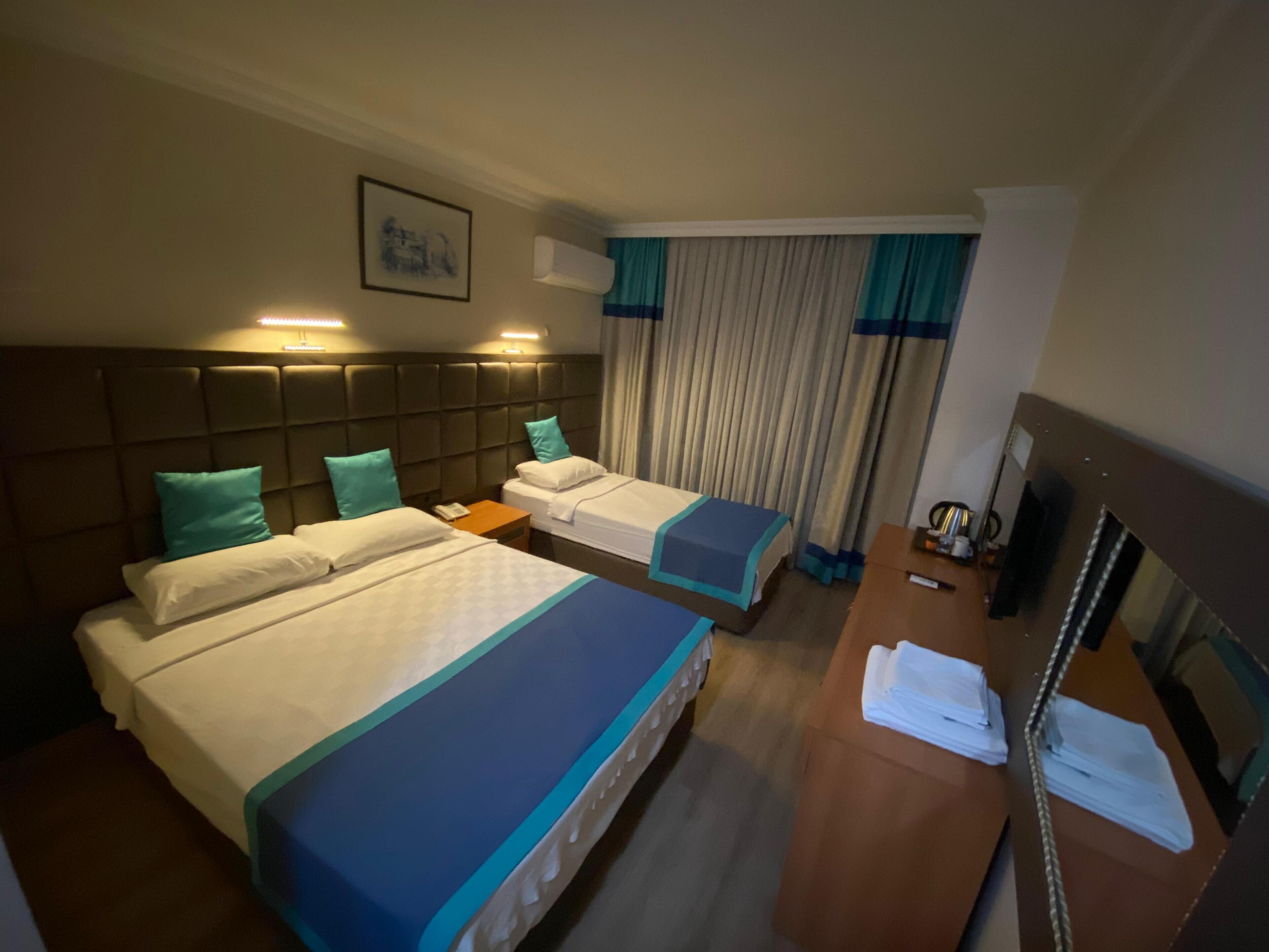 Habitación de hotel con dos camas, un escritorio, un espejo y una ventana con cortinas.