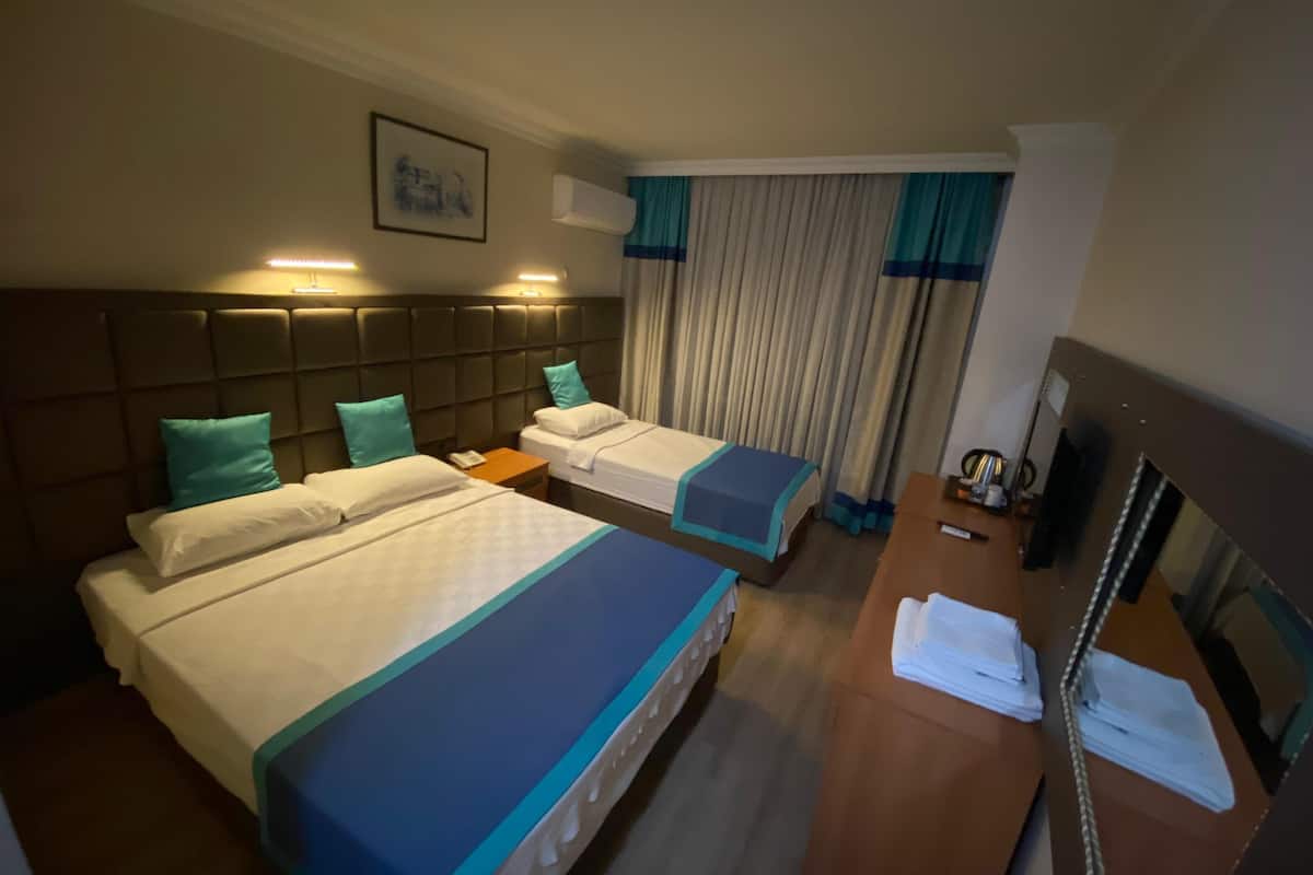 Habitación de hotel con dos camas, un escritorio, un espejo y una ventana con cortinas.