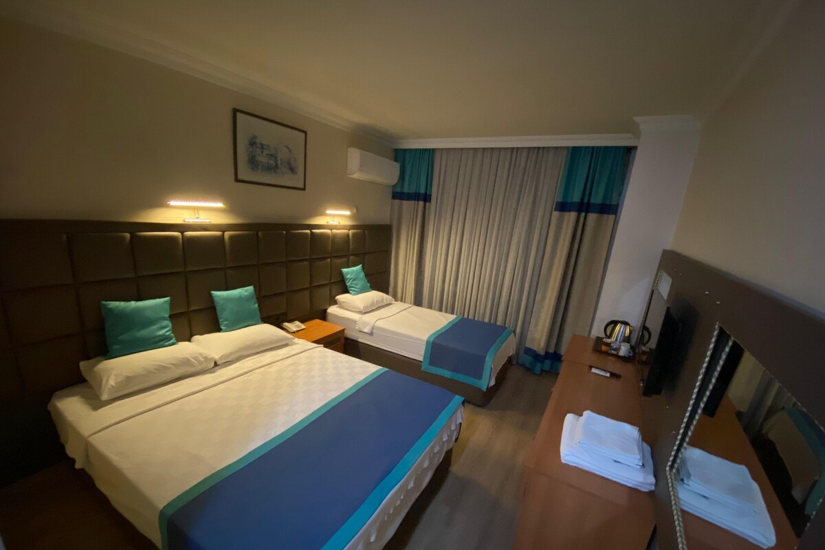 A hotel room with two beds, a desk, a mirror, and a window with curtains.