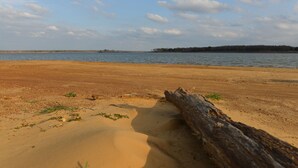 Une plage de sable avec un tronc d’arbre au premier plan et une étendue d’eau calme en arrière-plan.