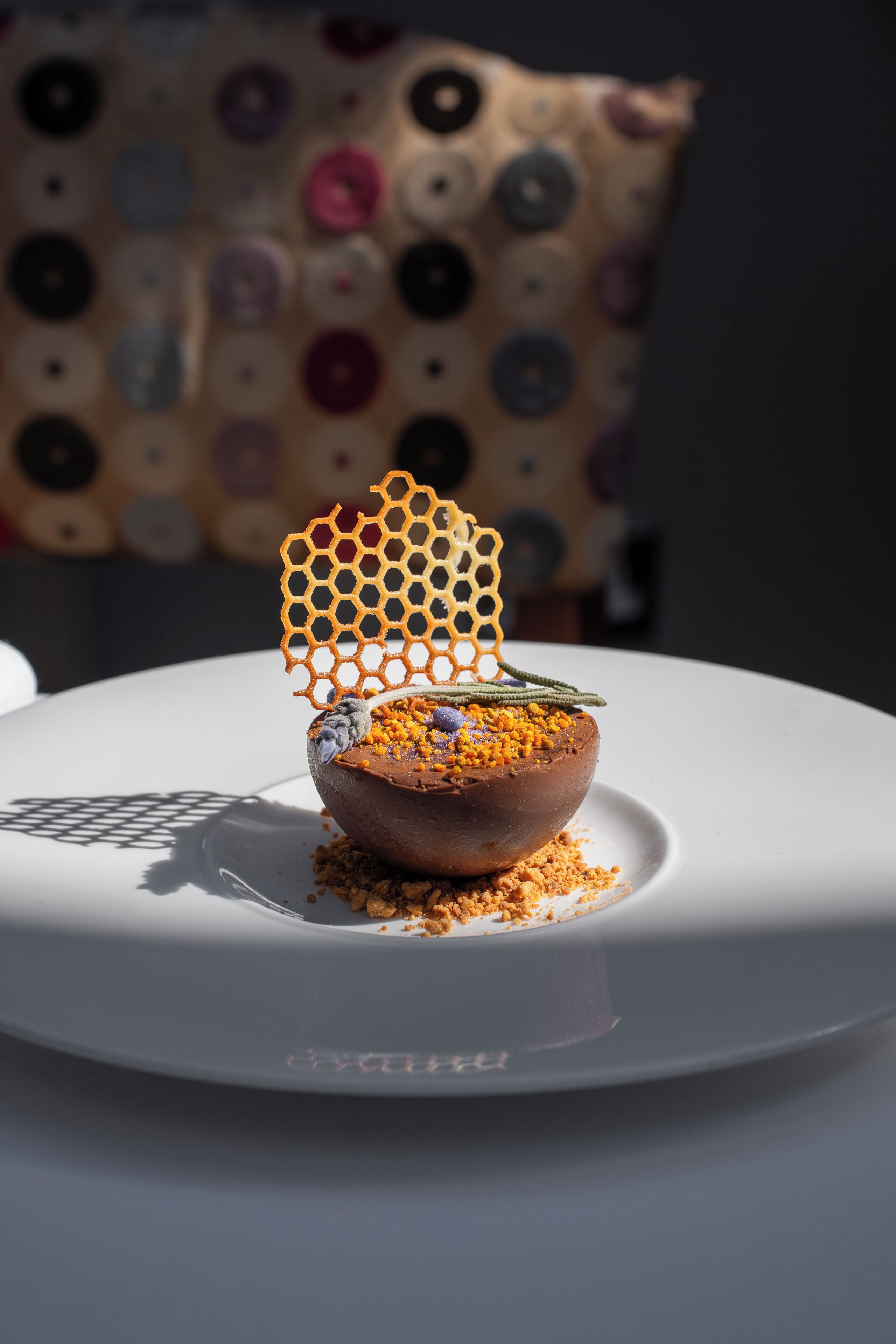 A dessert on a white plate with a honeycomb structure on top, placed on a table with a polka-dotted cloth in the background.