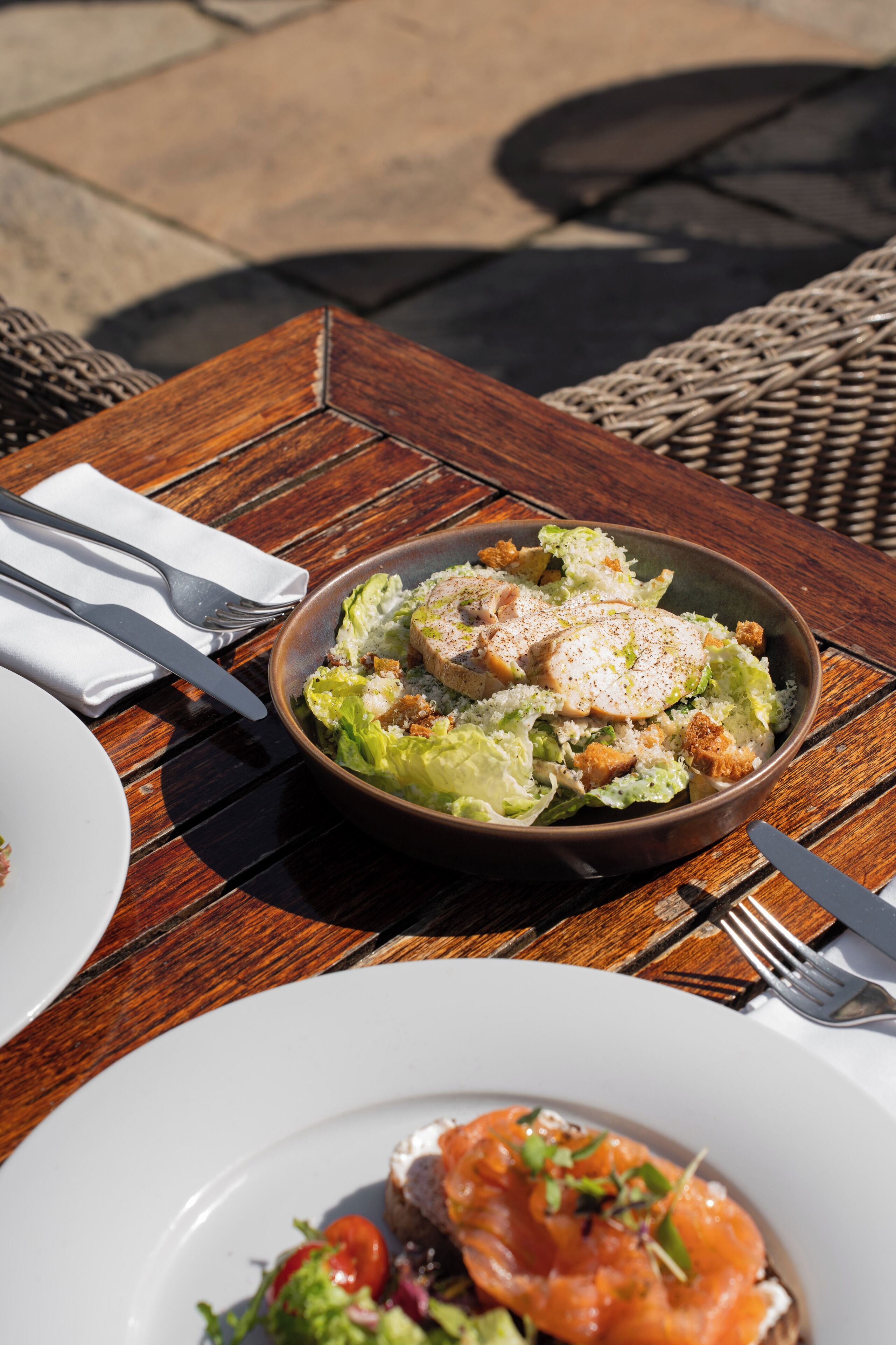 Een houten tafel met een saladeschaal en een bord eten.