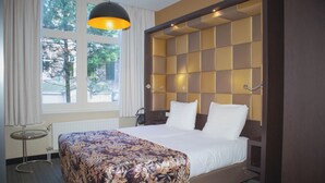 Une chambre d’hôtel avec un grand lit, une table de chevet, une fenêtre avec des rideaux et une vue sur les arbres à l’extérieur.