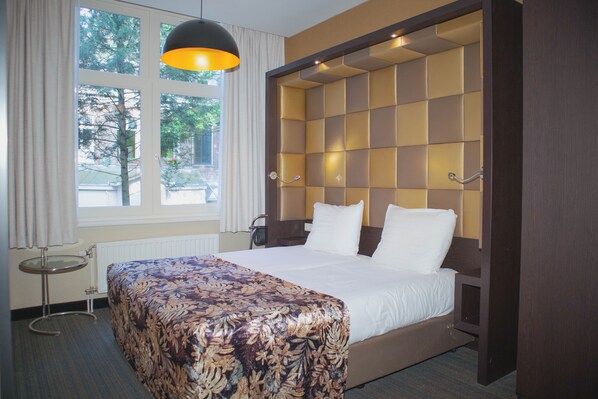 Een hotelkamer met een groot bed, een nachtkastje, een raam met gordijnen en uitzicht op bomen.