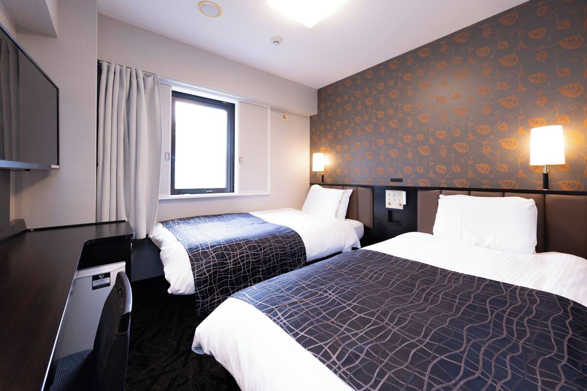 Ein Hotelzimmer mit zwei Betten, einem Fernseher, einem Fenster und einer Wand mit einem Blattmuster.