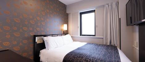 Habitación de hotel con cama, escritorio, ventana con cortinas, televisor y pared decorada con un diseño de hojas.