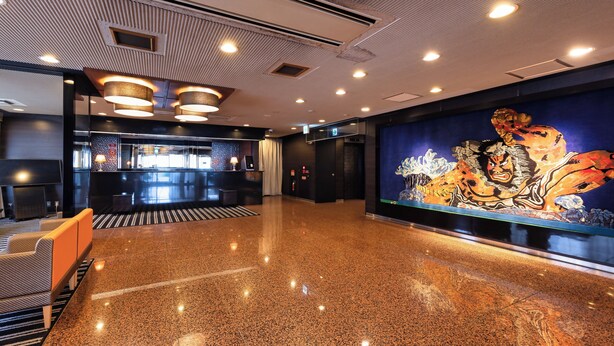 Een hotel lobby met een gepolijste granieten vloer, een receptiebalie en een groot muurdecoratie.